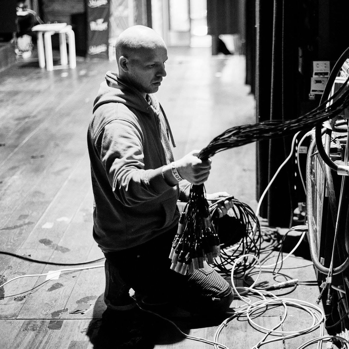 Riku kneeling on a stage, patching a multicore cable into a stage box